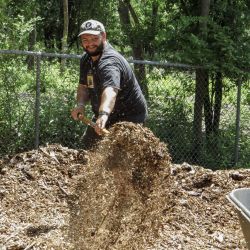 man outside picking up mulch with a rake