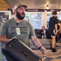 man holding a big speaker and cheering with a group of teens conversing in the background