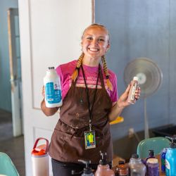 young adult female wearing an apron and holding paint supplies