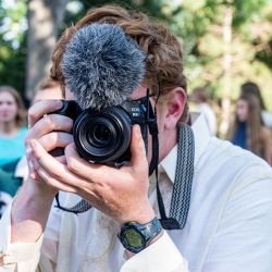 white male behind a camera with a mic on top