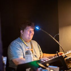 young adult male sitting at a sound board in a tech booth