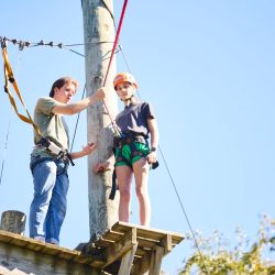 young adult male on top of zipline helping a student get ready to jump